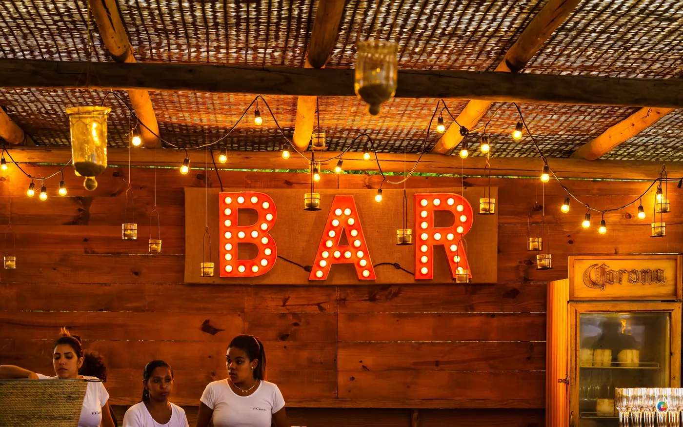 Red marquee letters spelling BAR glow against a wood wall hung with string lights