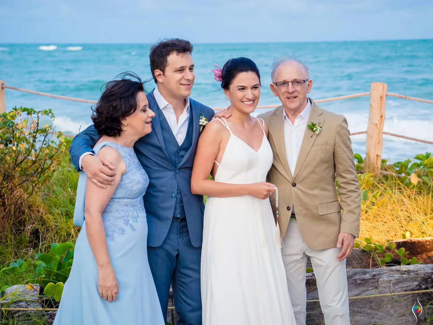 Evy and Thiago pose with a woman in pale blue and a man in a tan jacket, sea behind