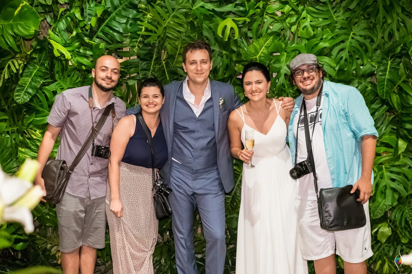 Evy and Thiago pose with three friends, two carrying cameras, in front of the leaf wall