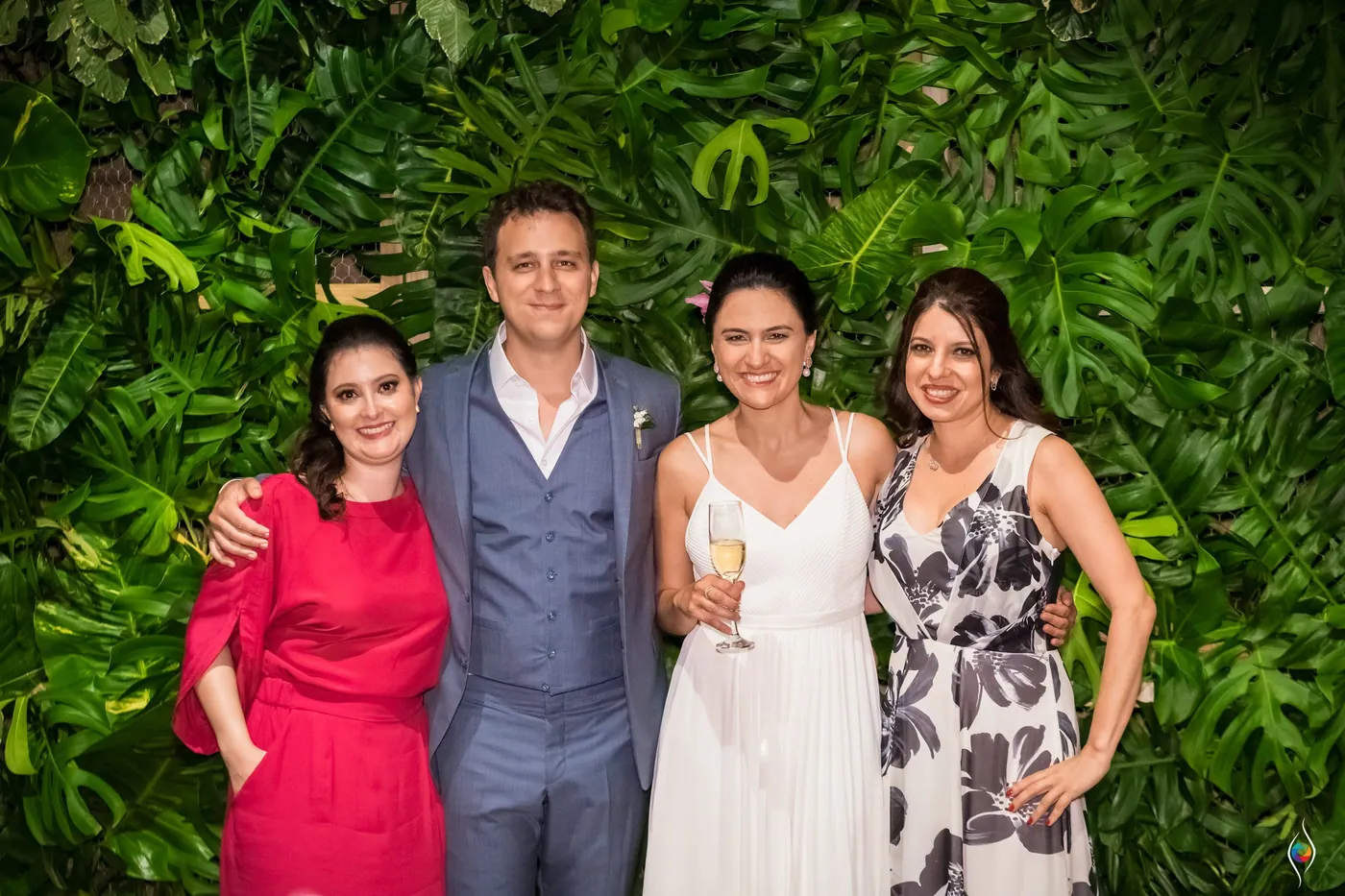 Thiago and Evy pose with two women in red and patterned dresses against the leaf wall