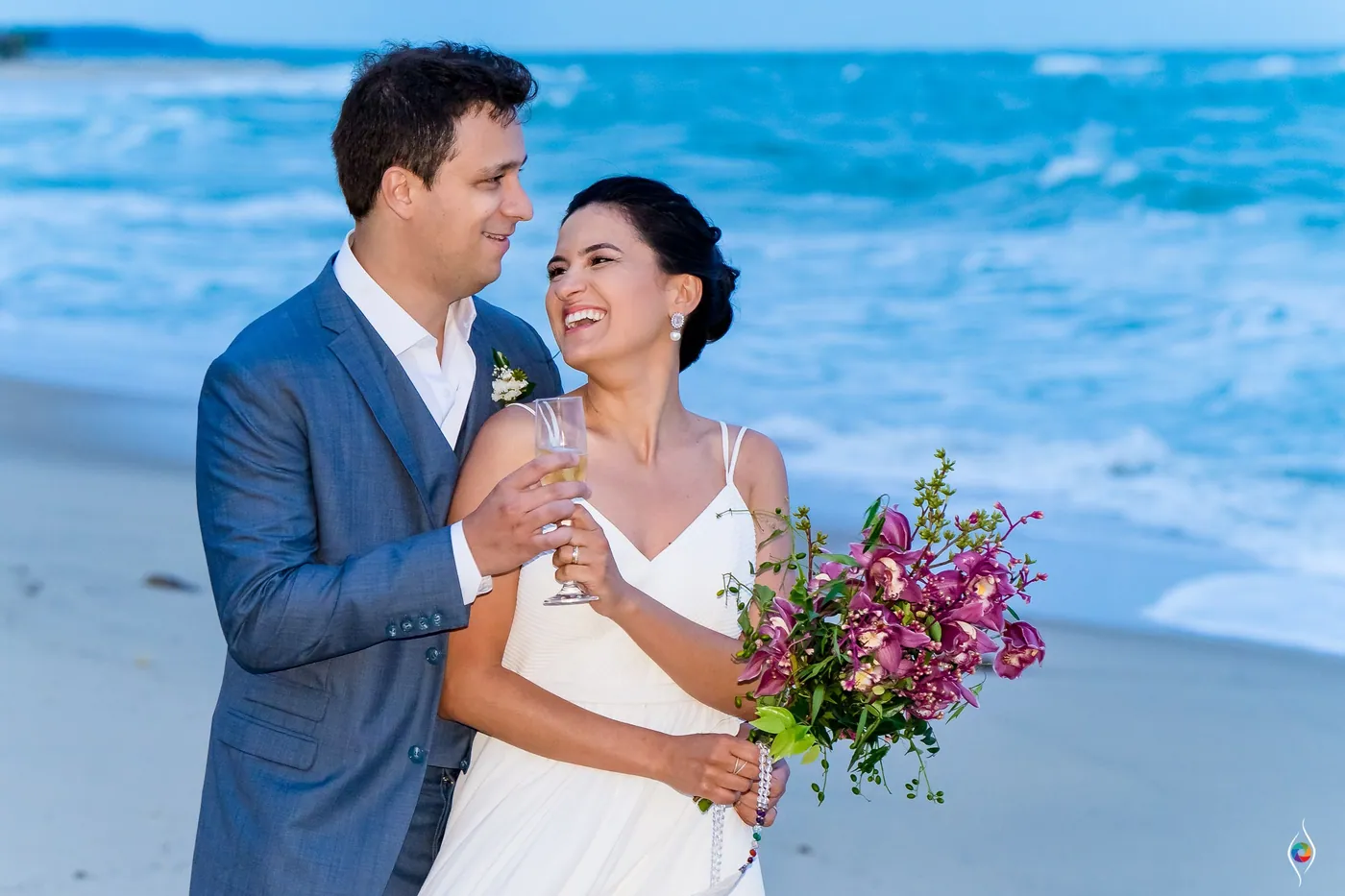 Evy and Thiago laugh into each other's eyes on the shore, a glass and her bouquet in their hands