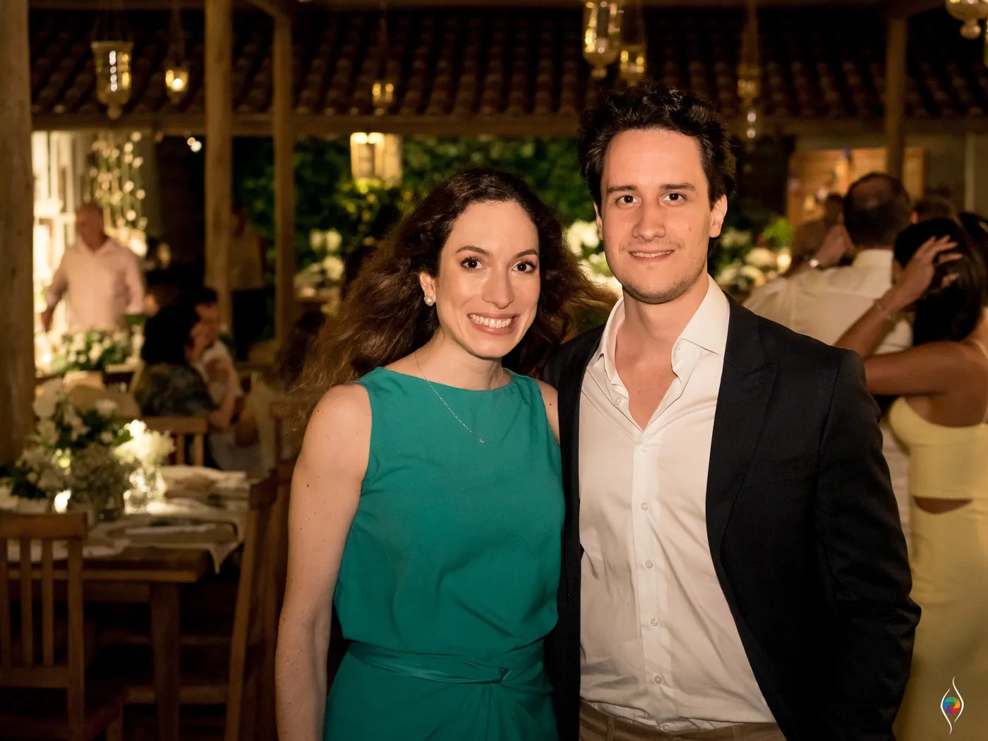 A woman in teal and a man in a dark jacket pose together at the reception, tables behind them