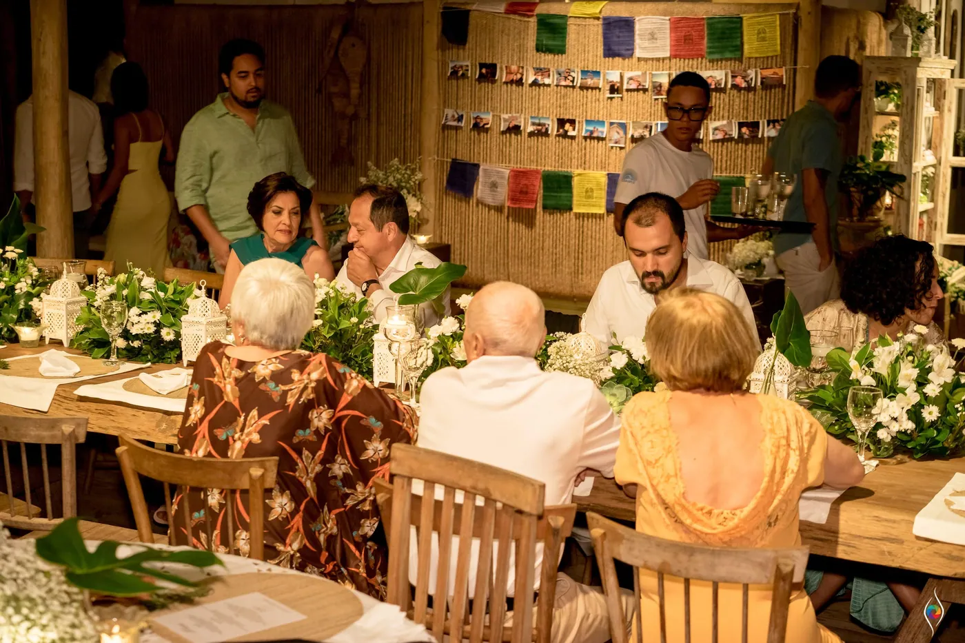 Guests sit at long wooden tables beneath a wall of photographs and prayer flags