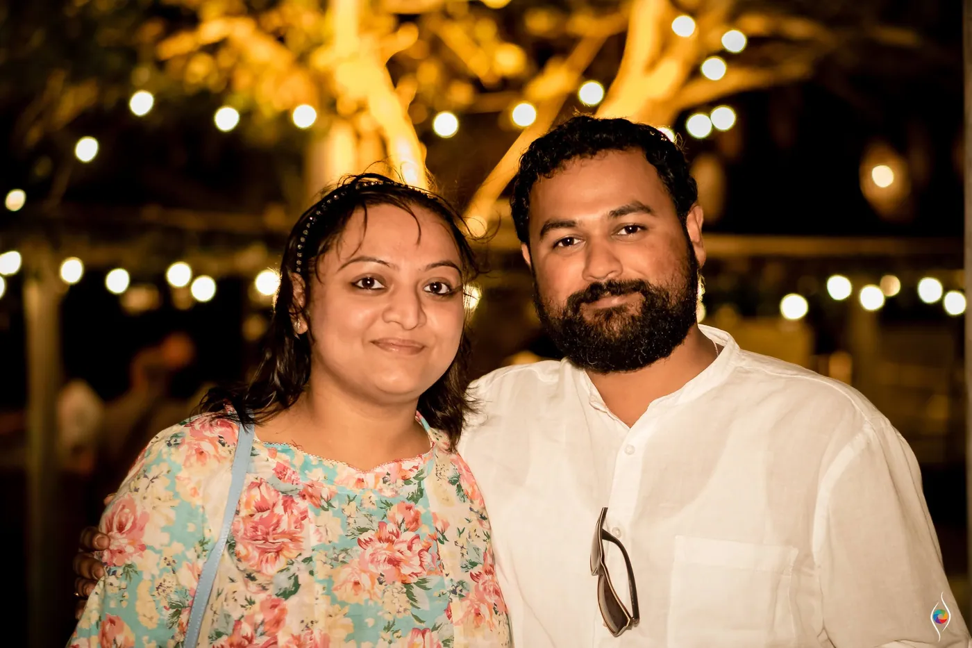 Two friends, a woman in florals and a bearded man in white, pose cheek to cheek