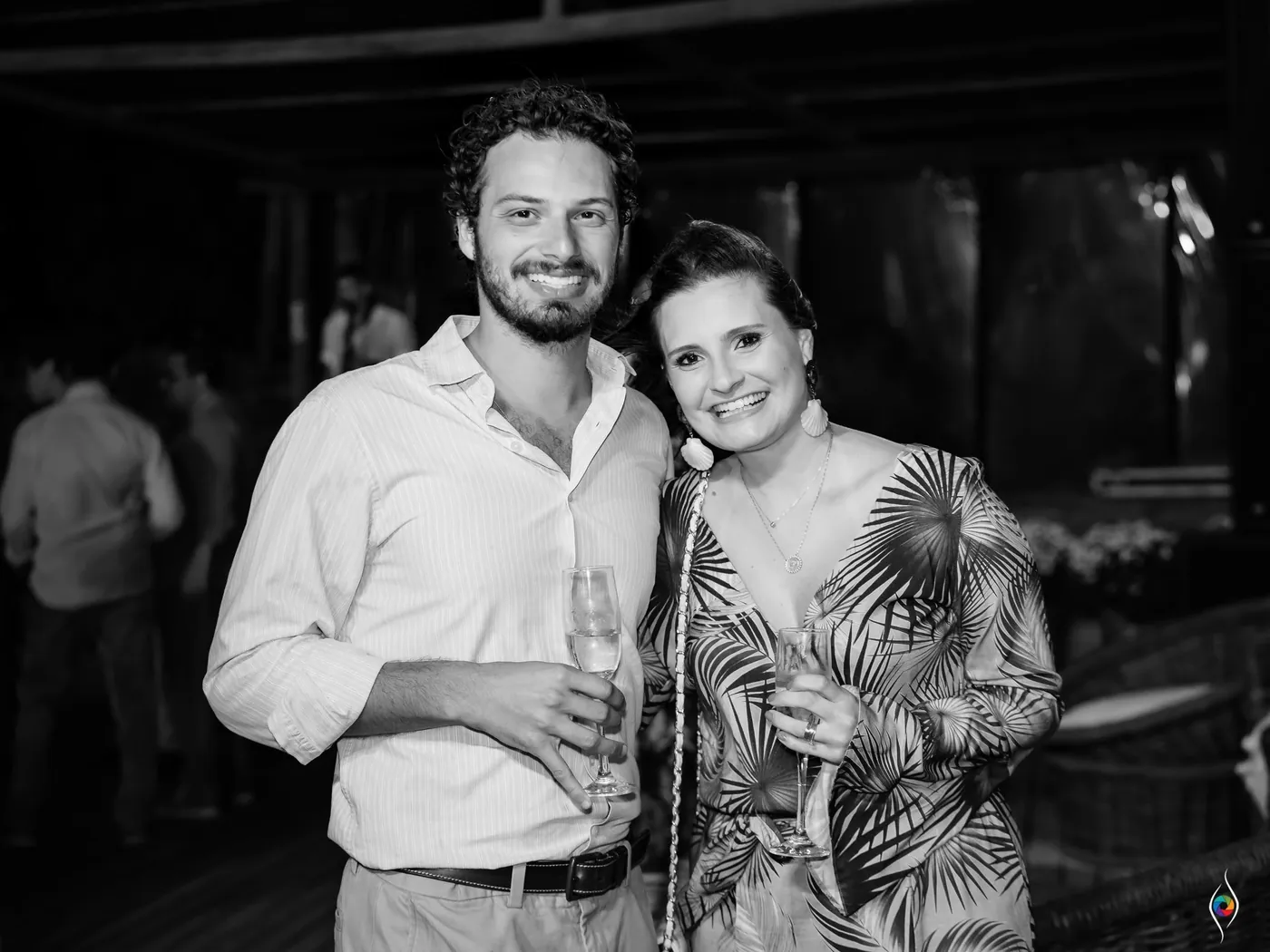 A man and a woman holding drinks pose close together in black and white