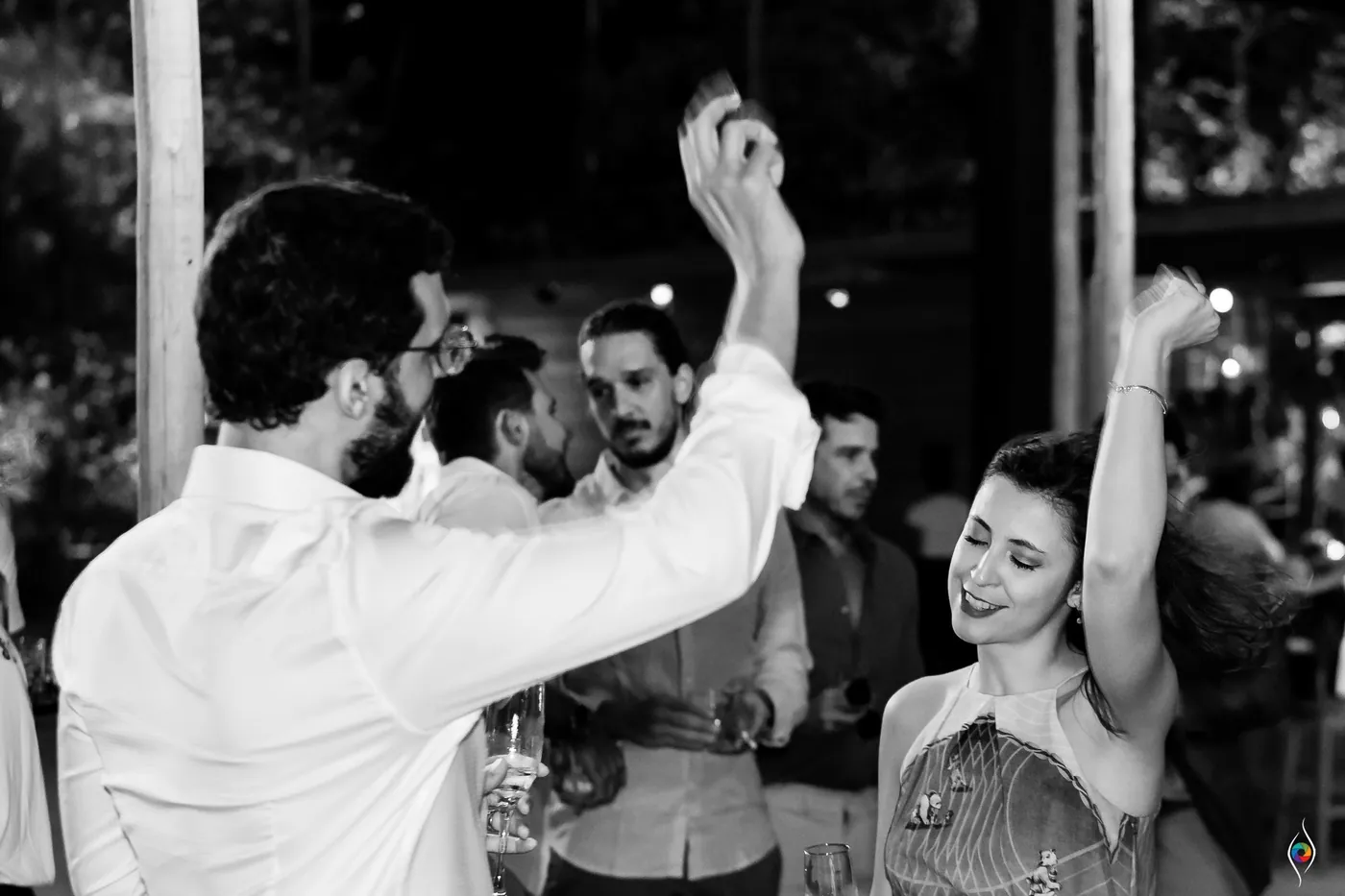 A man in white throws an arm up in black and white as friends dance close around him