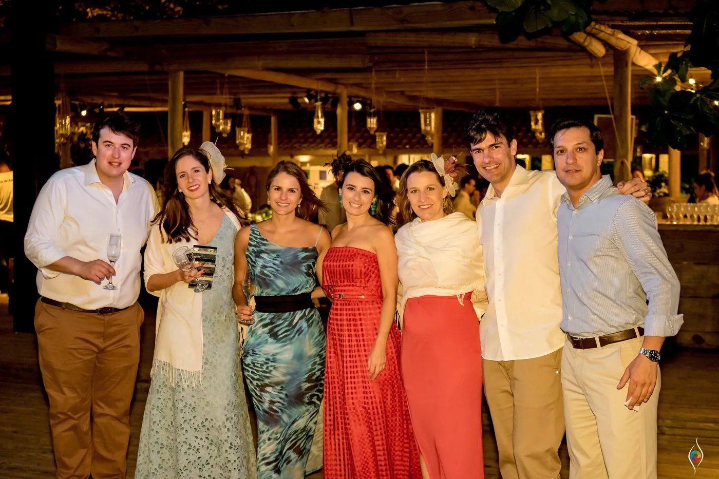 A line of guests in colourful dresses and light shirts smile for a group photo under warm lamps