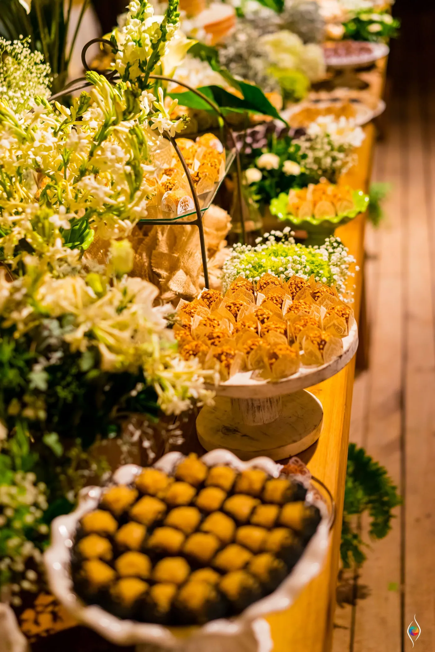 Trays of yellow sweets and savoury bites sit among white flowers on a lit table