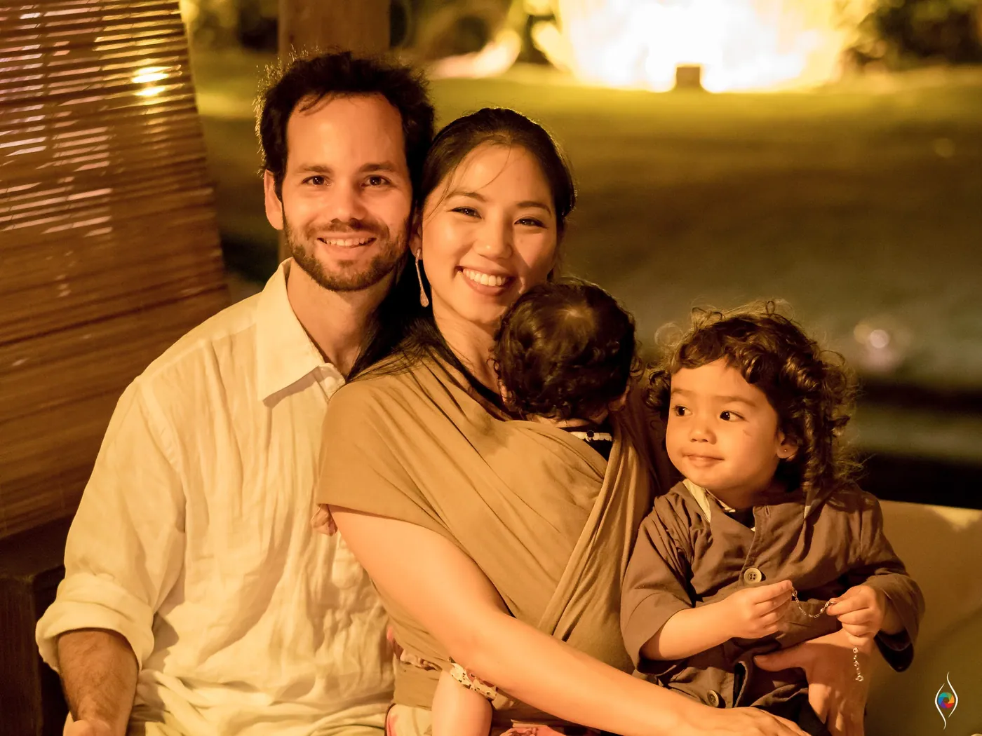 A man, a woman and a toddler sit close together in warm light, the adults smiling at the camera