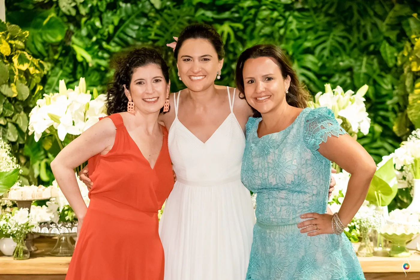 Evy in white stands between a woman in orange and a woman in turquoise, all with hands on hips