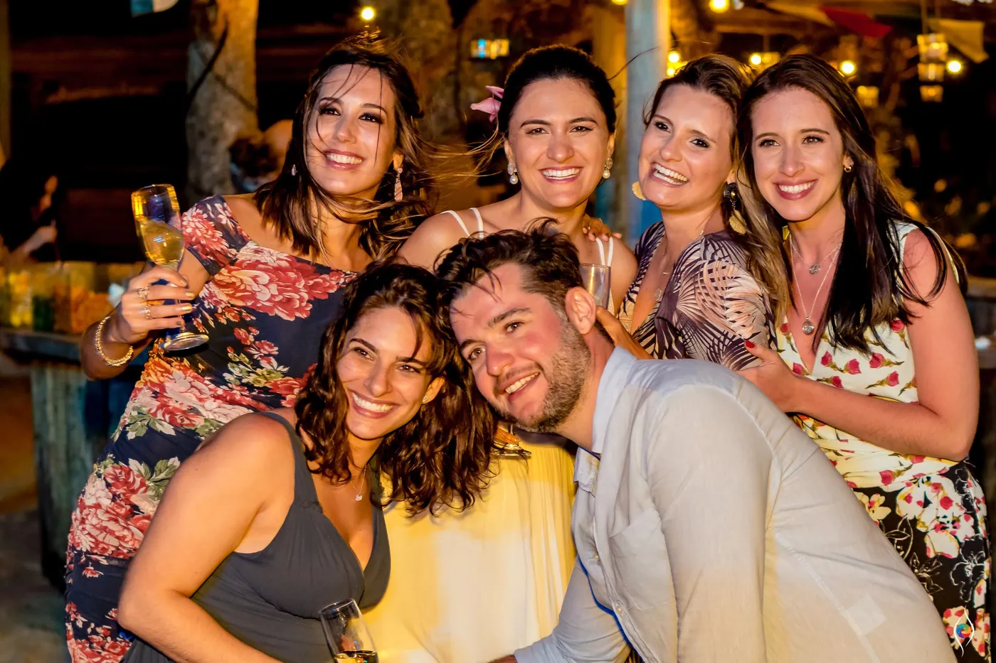 A knot of friends squeezes in for a laughing group shot, a man in a light jacket at the front